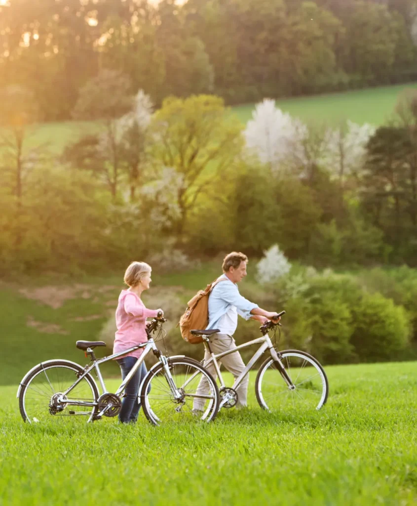 Coppia di adulti che camminano tenendo le biciclette in un prato verde di un parco